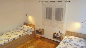 A small room with two wooden beds, a window with curtains, a nightstand, and a wall-mounted lamp. - Heated Infinity Pool, Family Apartment With Panoramic sea View 3 (Okrug)