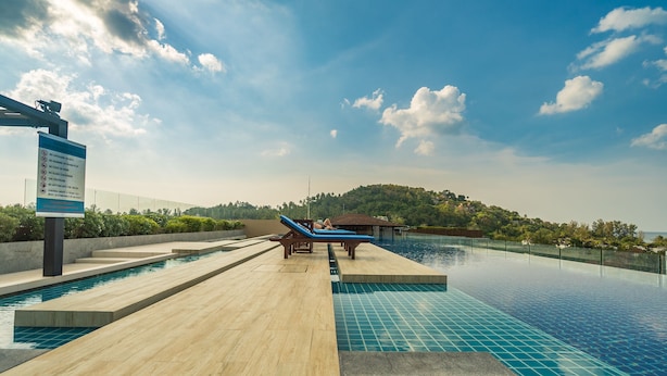 Zona de piscina con terraza de madera, sillas de descanso y un letrero.