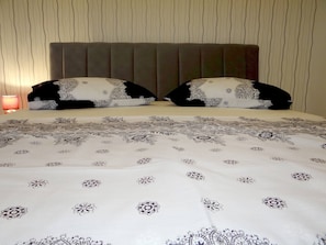 Uma cama com colcha estampada, duas almofadas com padrão preto e branco e um abajur ao lado.