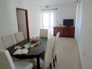 Un coin repas avec une table ronde, six chaises, un livre, deux bougies et une composition de fruits.