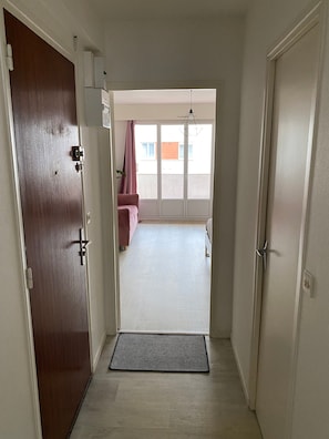 A hallway leading to a room with a large window, a door with a handle, and a doormat on the floor.