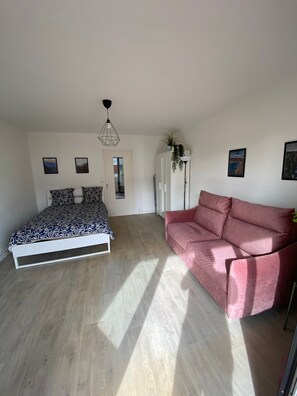 A bedroom with a bed, a pink sofa, a wardrobe, and a door leading to another room.