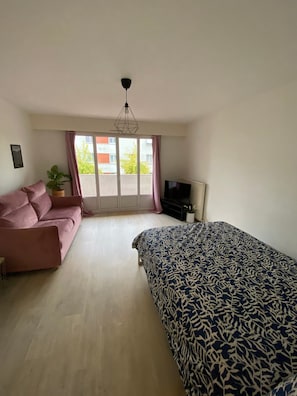 A bedroom with a bed, a sofa, a television, a potted plant, and a window with curtains.