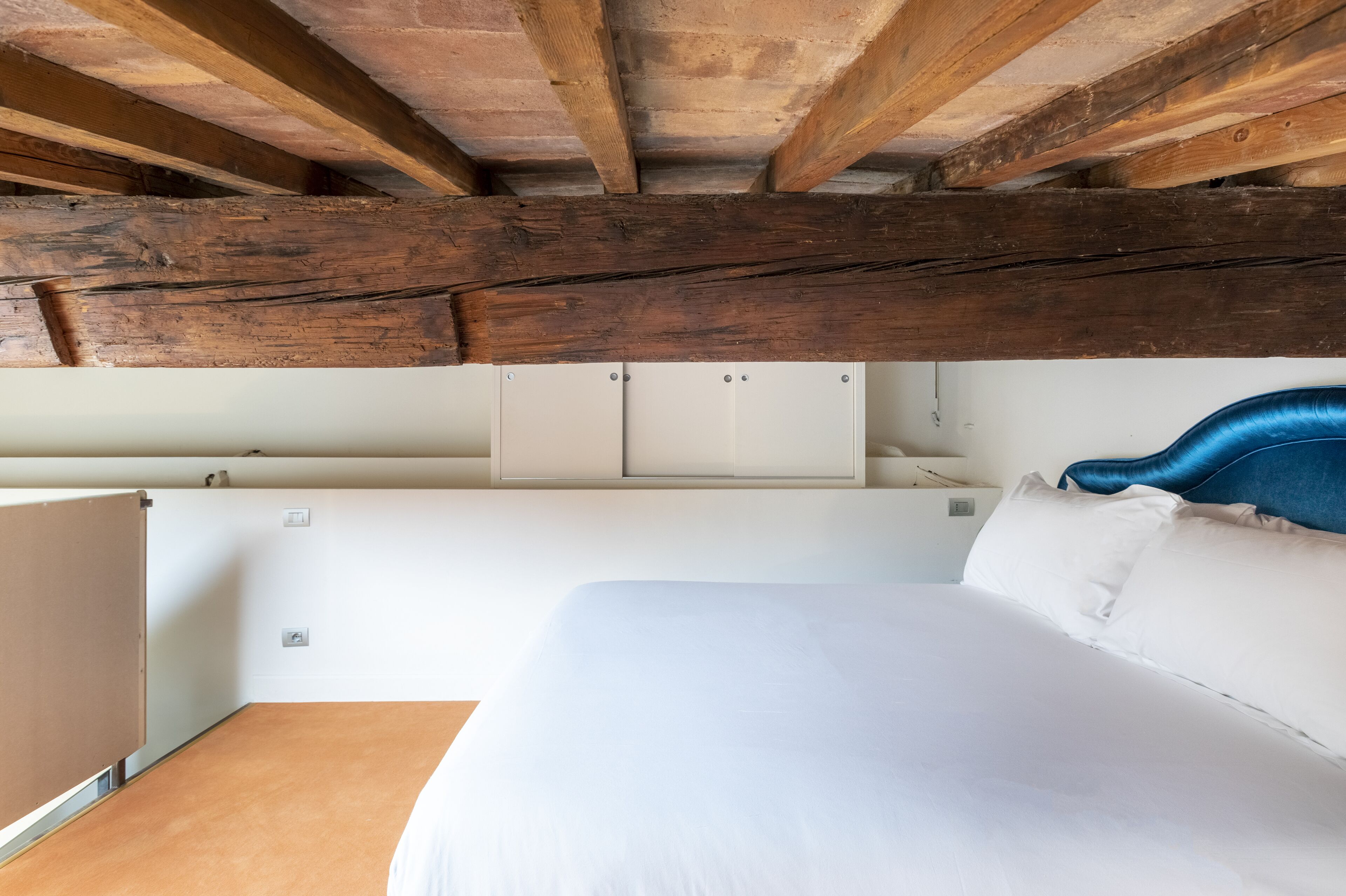 Une chambre avec un plafond en bois, des murs blancs, un lit avec une literie blanche et une tête de lit bleue.