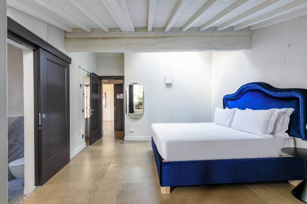 A bedroom with a large bed, a dark door, a mirror, and a hallway leading to another room.