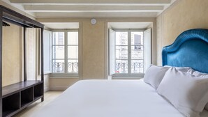 A hotel room with a large bed, a dark wooden bench, and two windows with balconies.