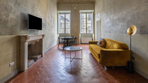 A room with a fireplace, a flat-screen TV, a yellow sofa, a round coffee table, and a floor lamp.