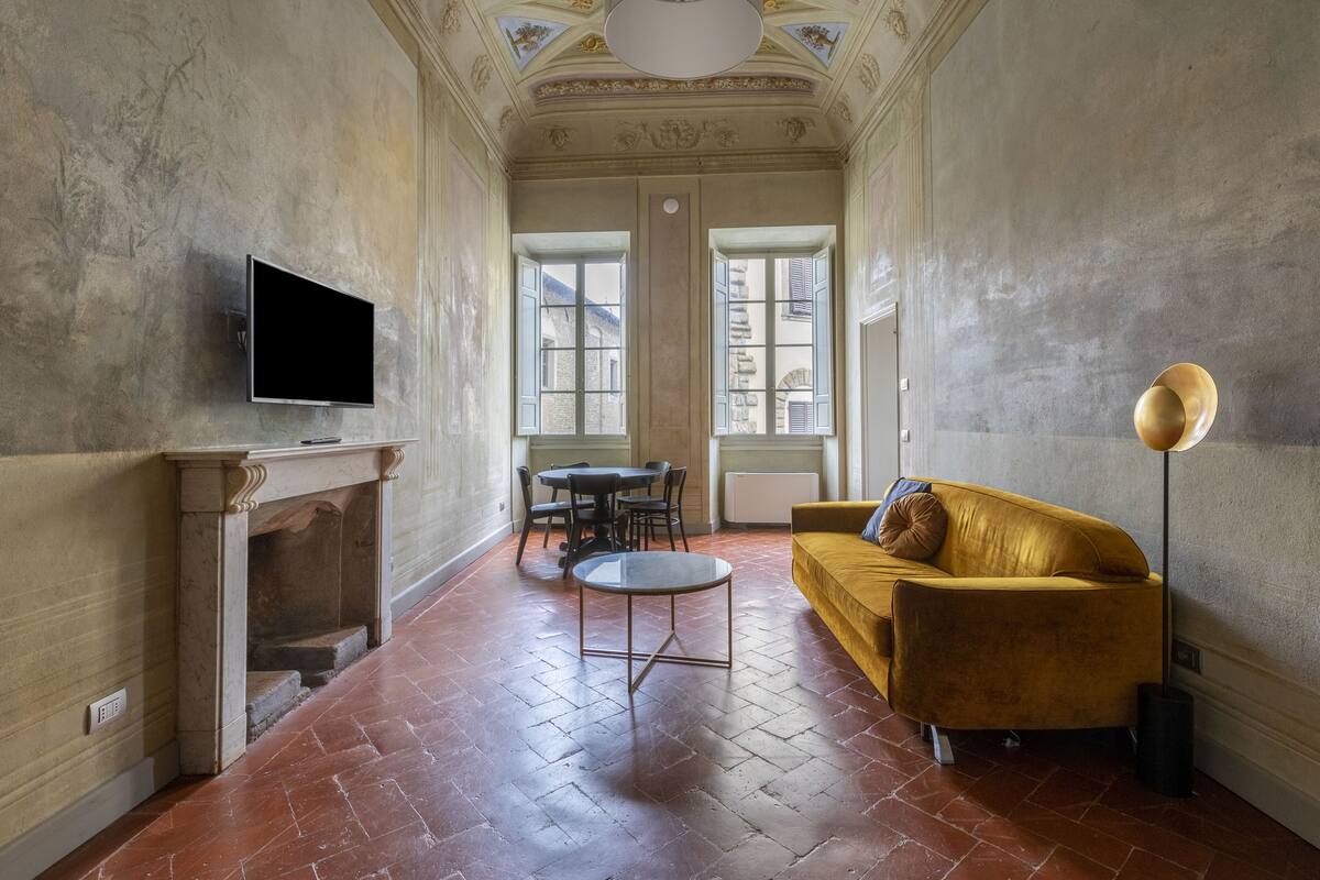 A room with a fireplace, a flat-screen TV, a yellow sofa, a round coffee table, and a floor lamp.