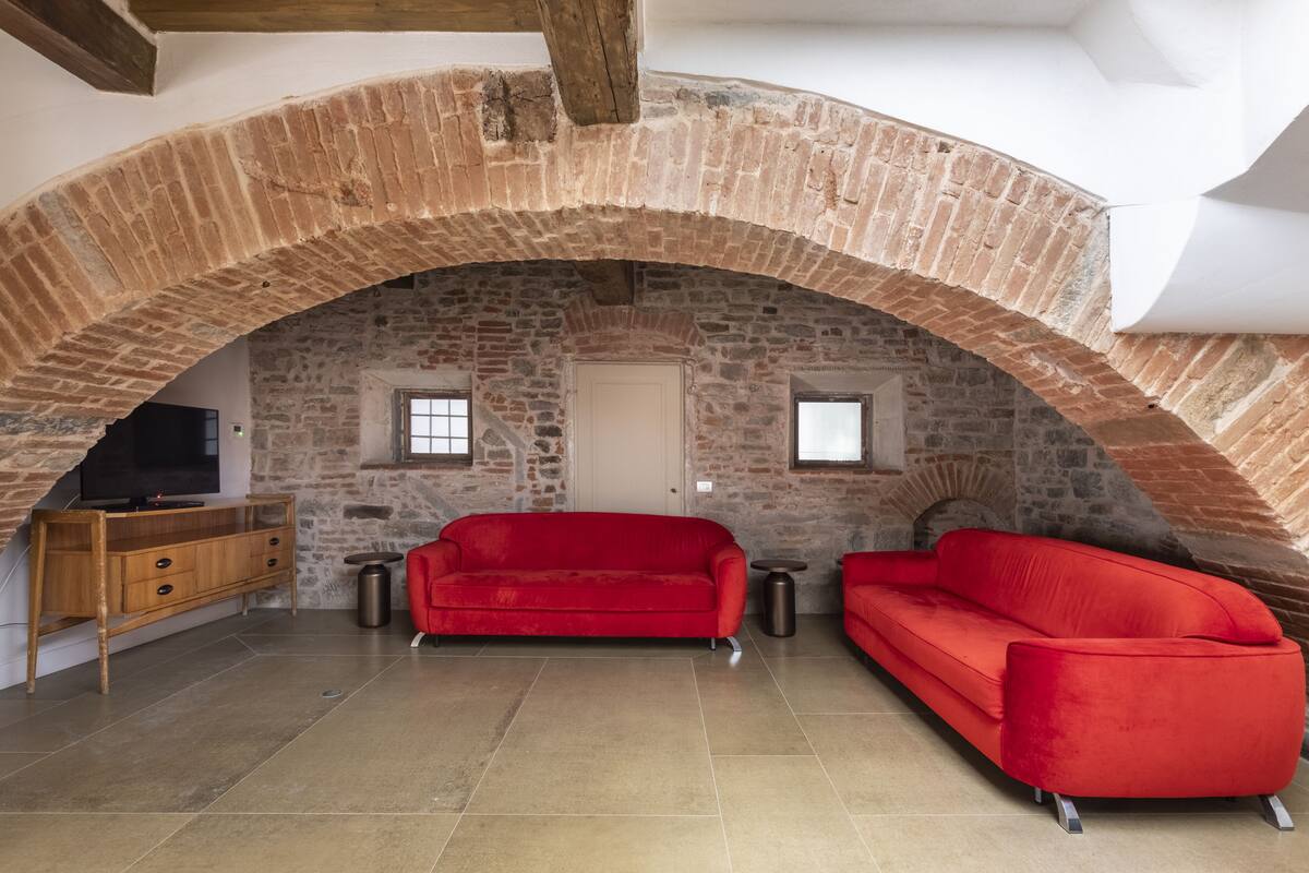 A room with a vaulted brick ceiling, two red sofas, a wooden cabinet, and a television.