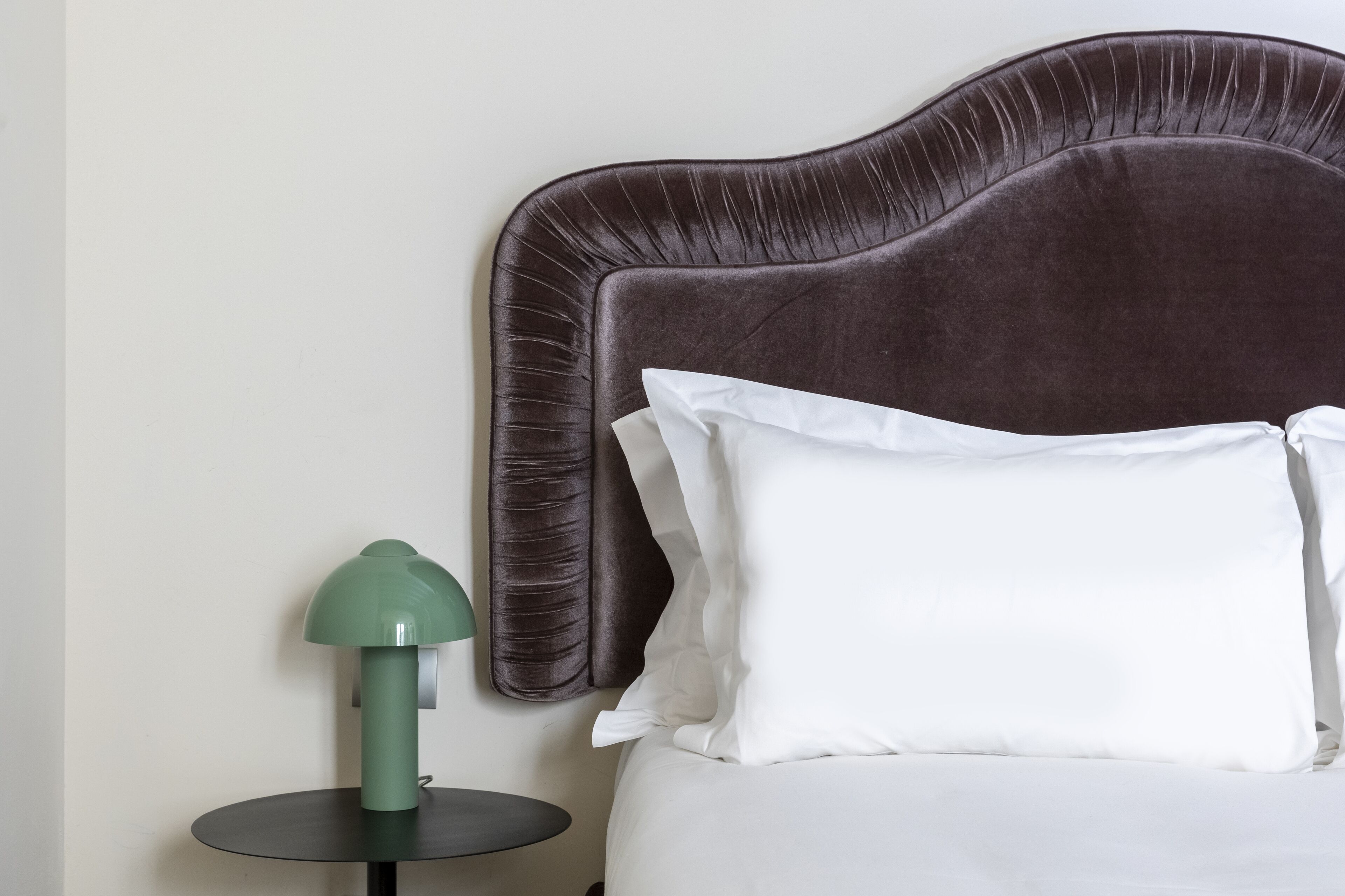 A bed with a dark headboard, white pillows, and a green lamp on a small table beside it.