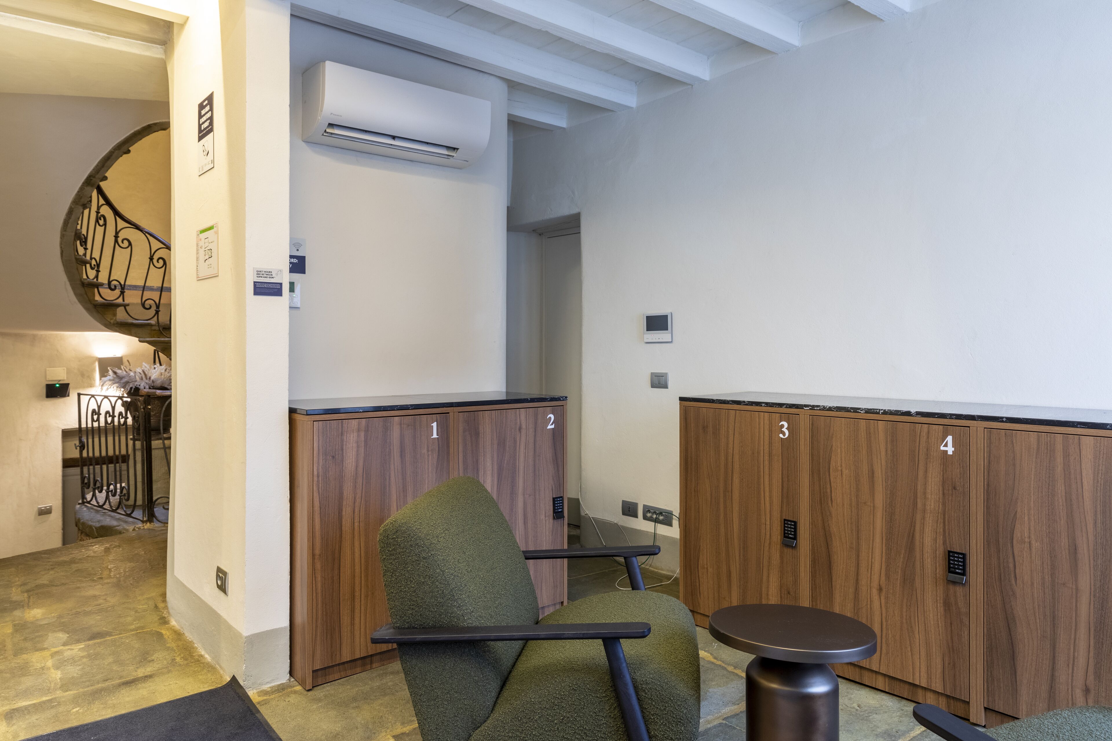 Ein Hotelzimmer mit einem Holzschrank, einem grünen Sessel, einem kleinen runden Tisch und einer Treppe mit Metallgeländer.