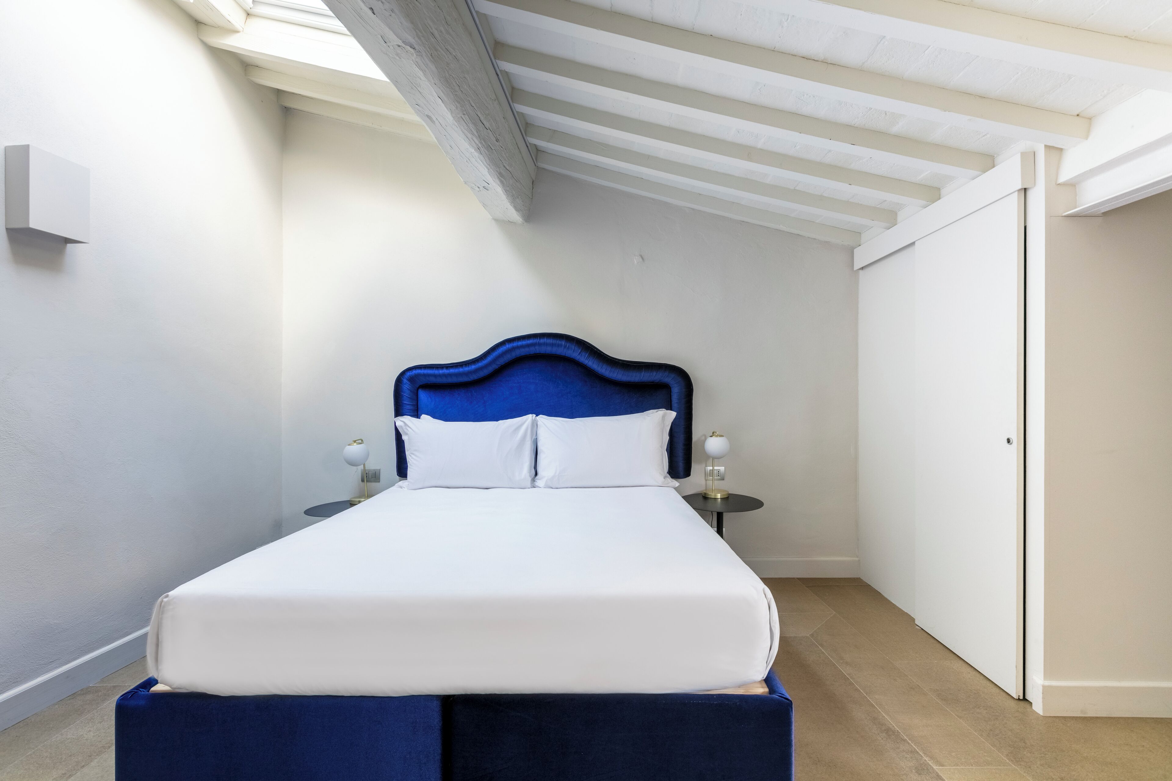 Ein Schlafzimmer mit Bett, Nachttischen, einem Kleiderschrank und einer geneigten Decke.