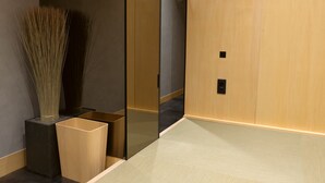 Un intérieur moderne avec un plancher en bois, un grand miroir et un grand vase contenant des roseaux.