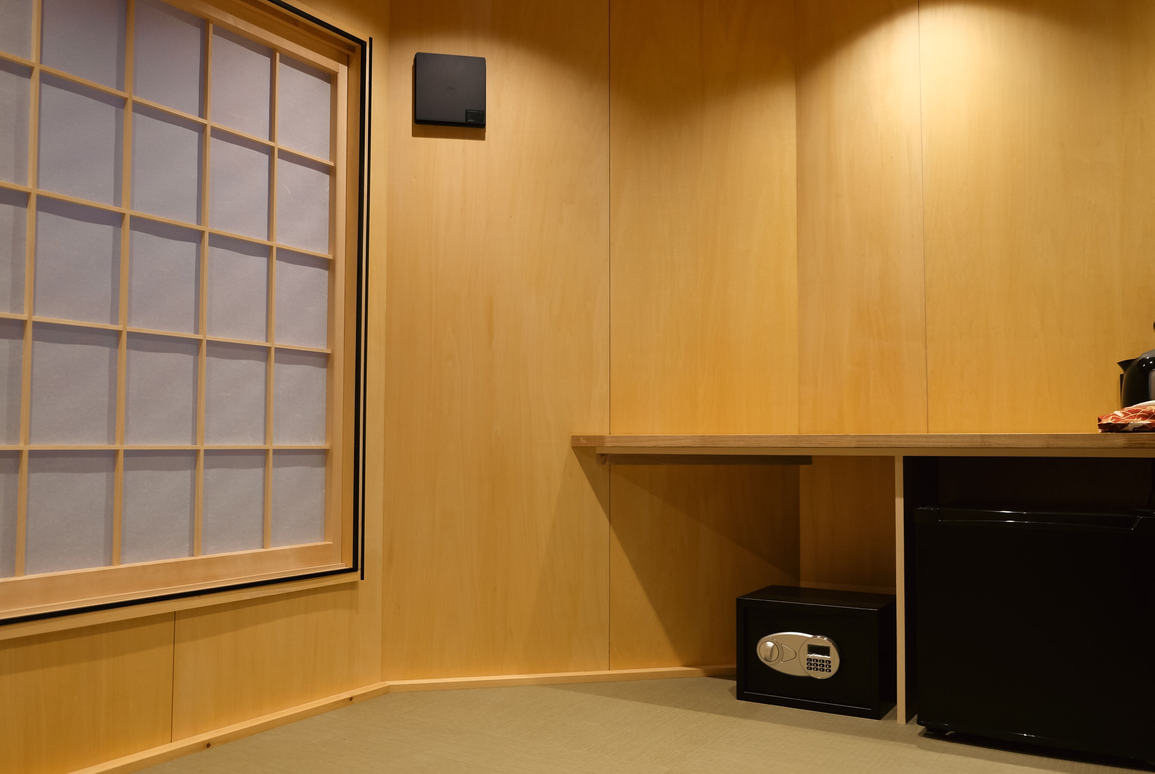 A room with wooden paneling, a large window with frosted glass, a black safe, and a small black appliance.