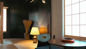 Une pièce avec un sol recouvert de tatamis, une lampe japonaise traditionnelle, une chaise bleue et une table ronde sur laquelle se trouve un objet rouge.