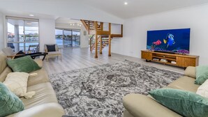 A spacious living room with a large TV, a staircase, and a view of the outside.