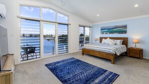 A bedroom with a large sliding glass door leading to a balcony, a bed with a wooden headboard, a nightstand, and a painting of a seascape.