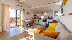 A living room with a sofa, coffee table, and a dining area with chairs and a table. There is a kitchen area with a stove, sink, and cabinets. - Apartment 'Gîte Durance' with Mountain View, Wi-Fi and Air Conditioning (Mallemort)