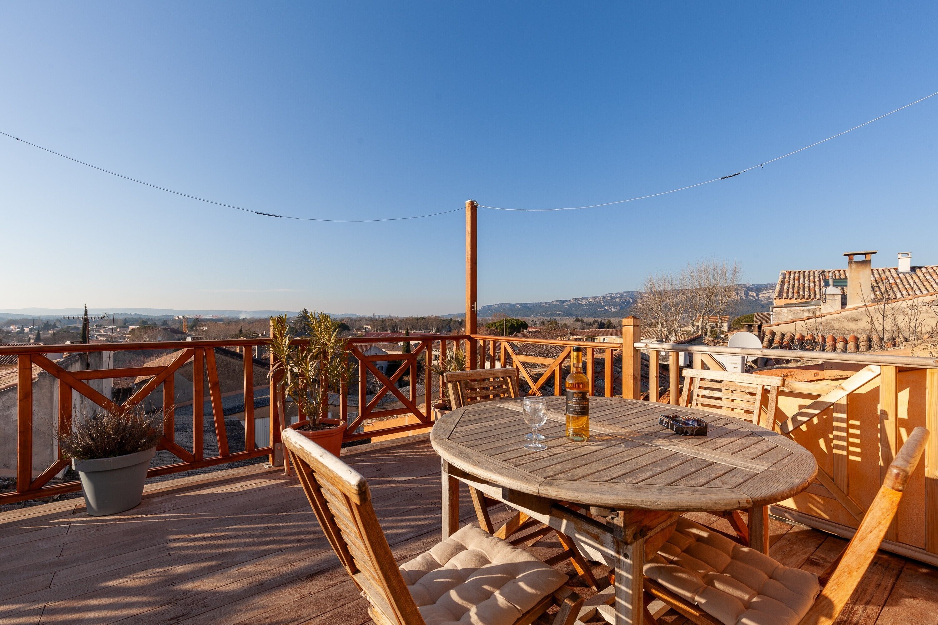 Eine Holzterrasse mit einem runden Tisch und Stühlen, einem Blumentopf und Blick auf die Stadt im Hintergrund.