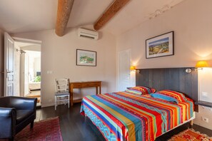 A bedroom with a bed, a desk, a chair, and a door leading to another room.