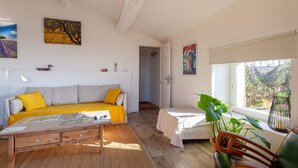 A room with a sofa, a small table, a window with plants, and artwork on the walls. - Apartment 'Gîte Durance' with Mountain View, Wi-Fi and Air Conditioning (Mallemort)