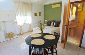 A dining area with a table, chairs, a vase with flowers, and a bed with pillows in the background. - Small stone house in a quiet place island Solta (Stomorska)