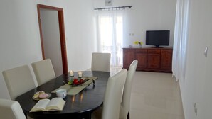 A dining area with a round table, six chairs, a book, two candles, and a fruit arrangement. - Heated infinity pool, family apartment with panoramic sea view 2 (Okrug Gornji)