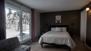 A bedroom with a large window, a bed, a chair, and a small table. - One Bedroom Condo Near Whyte Ave (Edmonton)