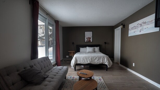 A bedroom with a bed, a sofa, a small table, and a window with curtains. - One Bedroom Condo Near Whyte Ave (Edmonton)