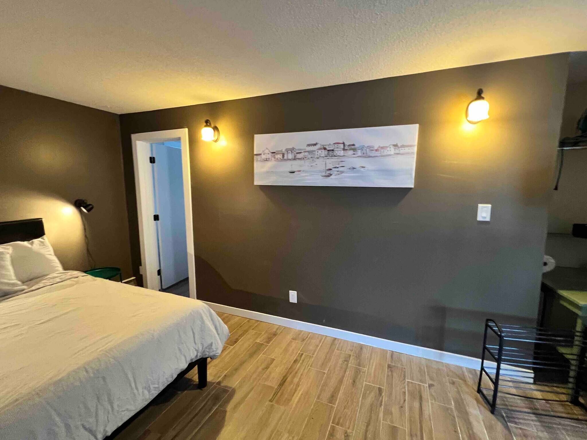 A bedroom with a bed, a door, a wall-mounted picture, and a small table.