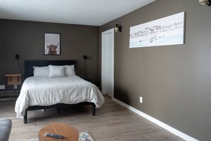 Un dormitorio con una cama, una mesita de noche, una lámpara, un cuadro y vistas al exterior.