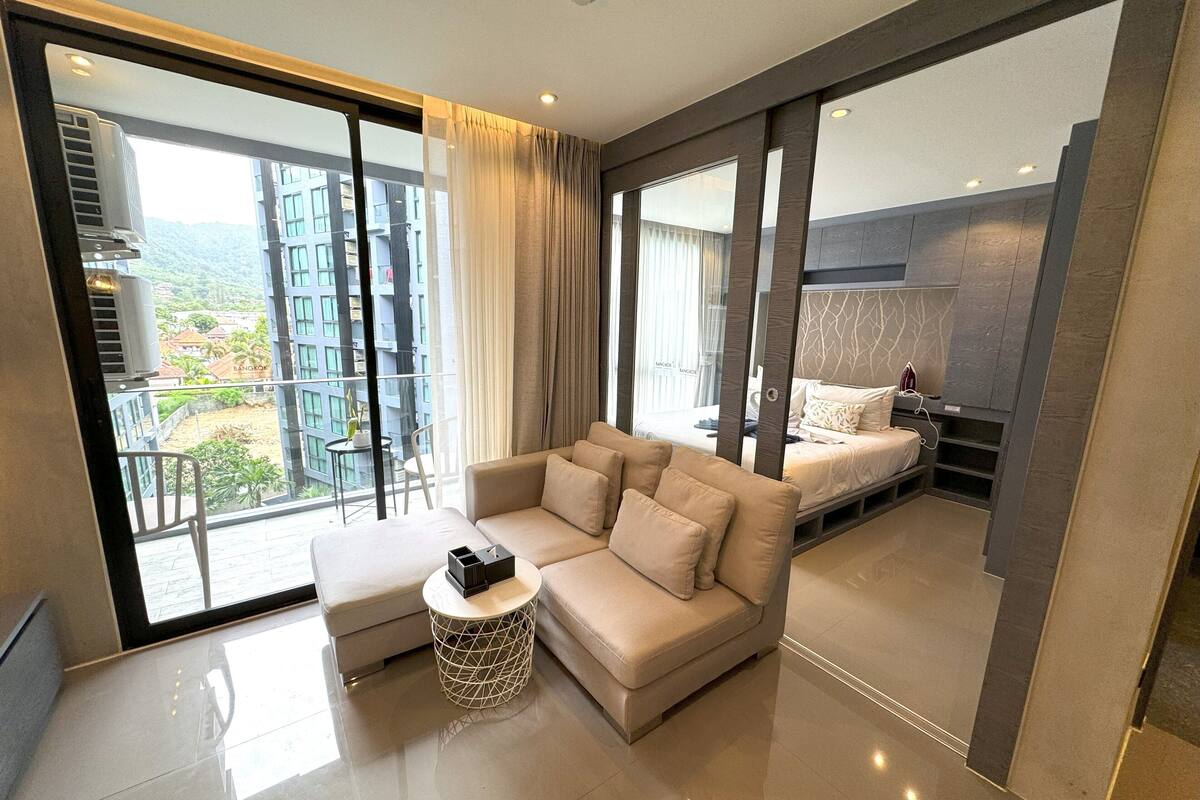 A modern hotel room with a large window, a sofa, a bedside table, and a bed.