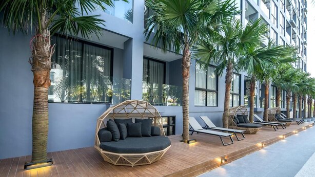 Un área de descanso al aire libre moderna con terraza de madera, asientos de mimbre y palmeras.