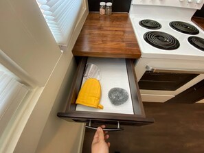 Una cocina con estufa blanca, encimera de madera y un cajón con un paño amarillo y un objeto de vidrio.