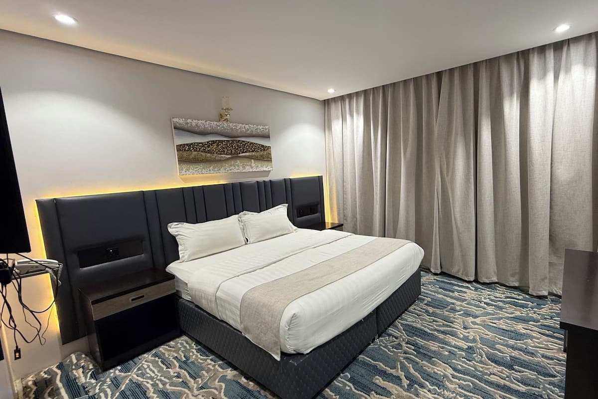 Une chambre d’hôtel moderne, dotée d’un grand lit, d’une table de chevet, d’un bureau et d’un téléviseur fixé au mur.