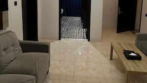 A modern living room with a sofa, a coffee table, and a TV. There is a hallway leading to a bathroom with a shower curtain. - QIMAM PARK 4 Abha (Abha)