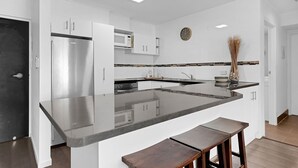 Une cuisine moderne avec des meubles blancs, un réfrigérateur en acier inoxydable, un four à micro-ondes et un grand îlot central doté de tabourets de bar.