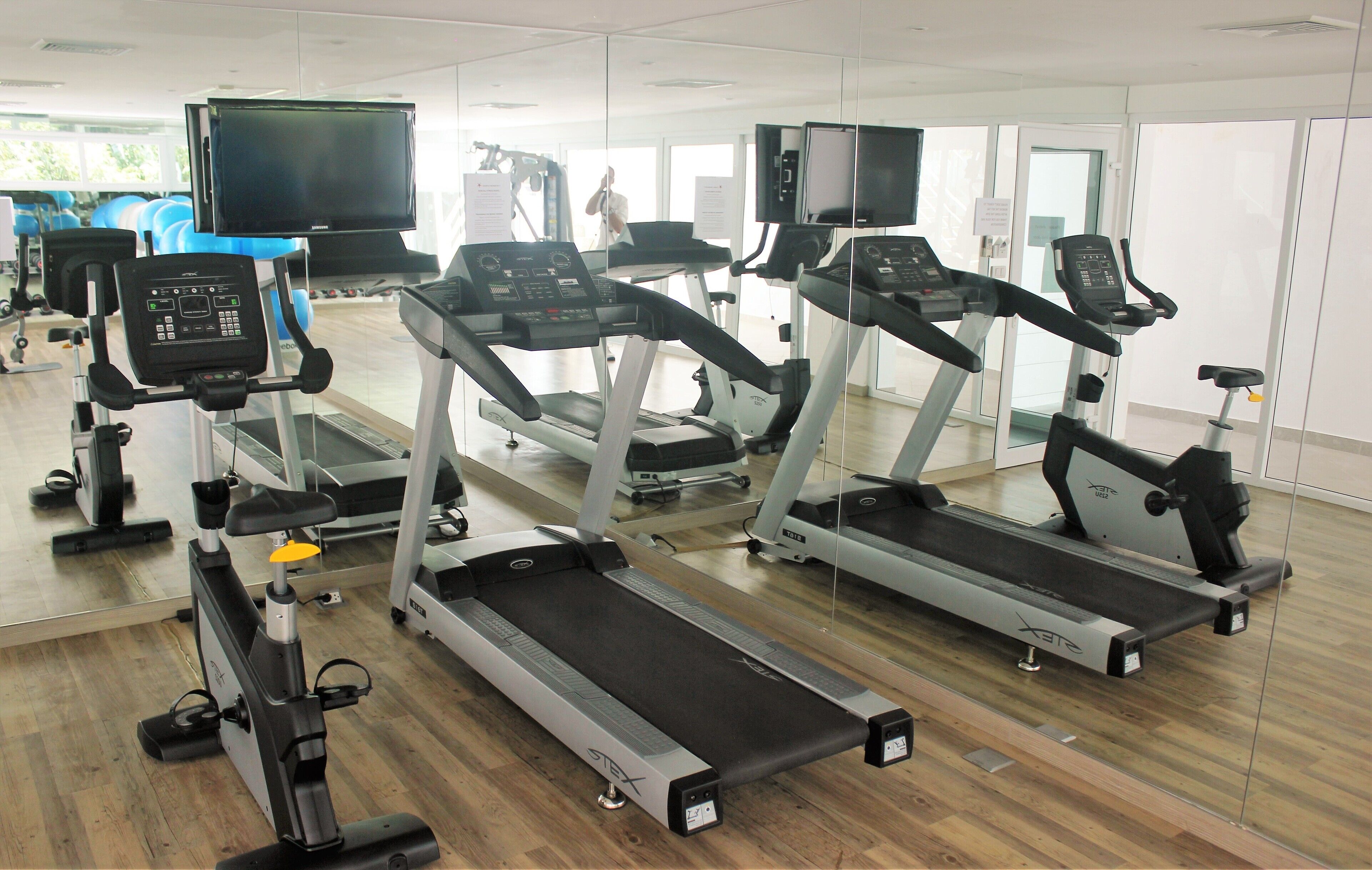 A gym with multiple treadmills, exercise bikes, and a mirrored wall.
