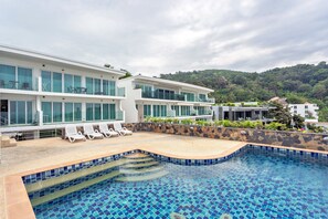 Un hôtel moderne doté d’une piscine, de chaises longues et offrant une vue sur une colline verdoyante.
