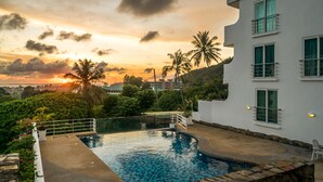 A swimming pool with a view of a sunset, a white building, and palm trees. - Apartment at Kata Ocean View by Lofty (Karon)