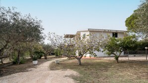 Un edificio de fachada blanca, un sendero de grava y árboles en primer plano.