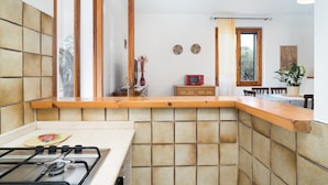 Una cocina con estufa a gas, encimera de madera, salpicadero de azulejos y comedor con sillas y una mesa.