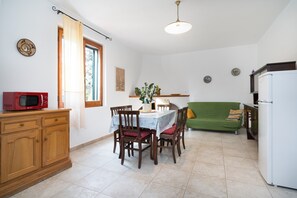 Una cocina compacta con una mesa de comedor, sillas, microondas, refrigerador y un sofá verde.