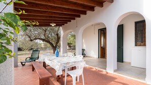 Un patio techado con una mesa y sillas, un banco y una puerta que da a una habitación.