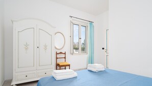 Un dormitorio con cama, armario, silla, ventana y puerta.