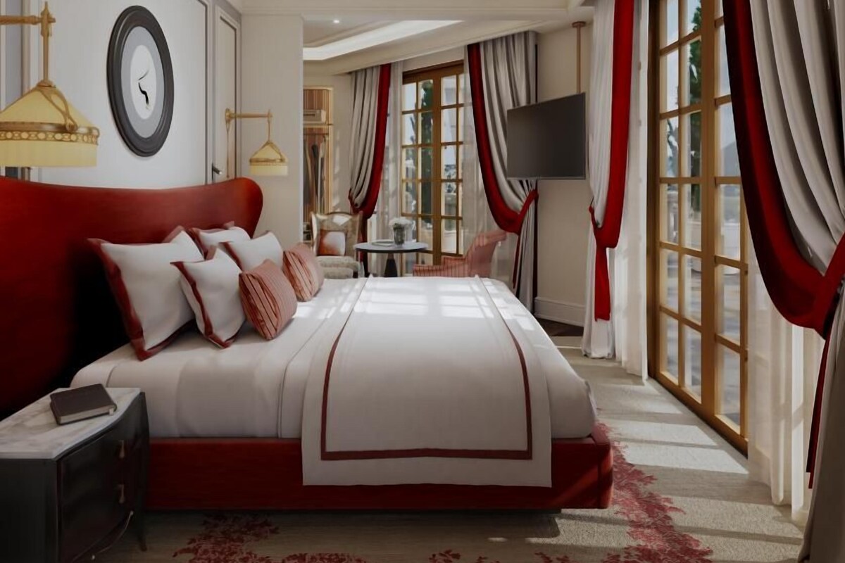 A spacious bedroom with a large bed, a bedside table, a TV, and a window with curtains.