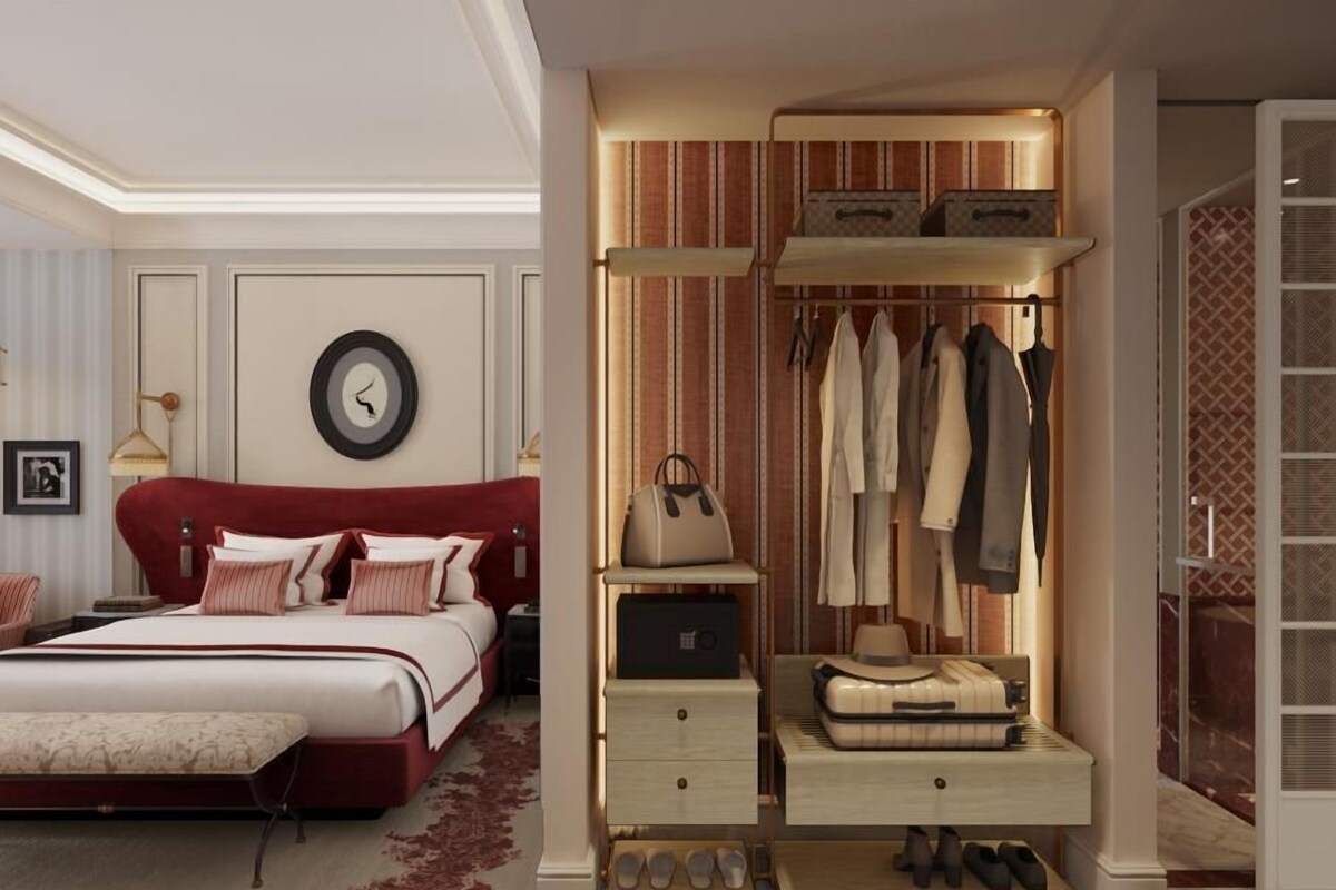 A bedroom with a red upholstered bed, a bedside table, a wardrobe with hanging clothes, and a shoe rack.