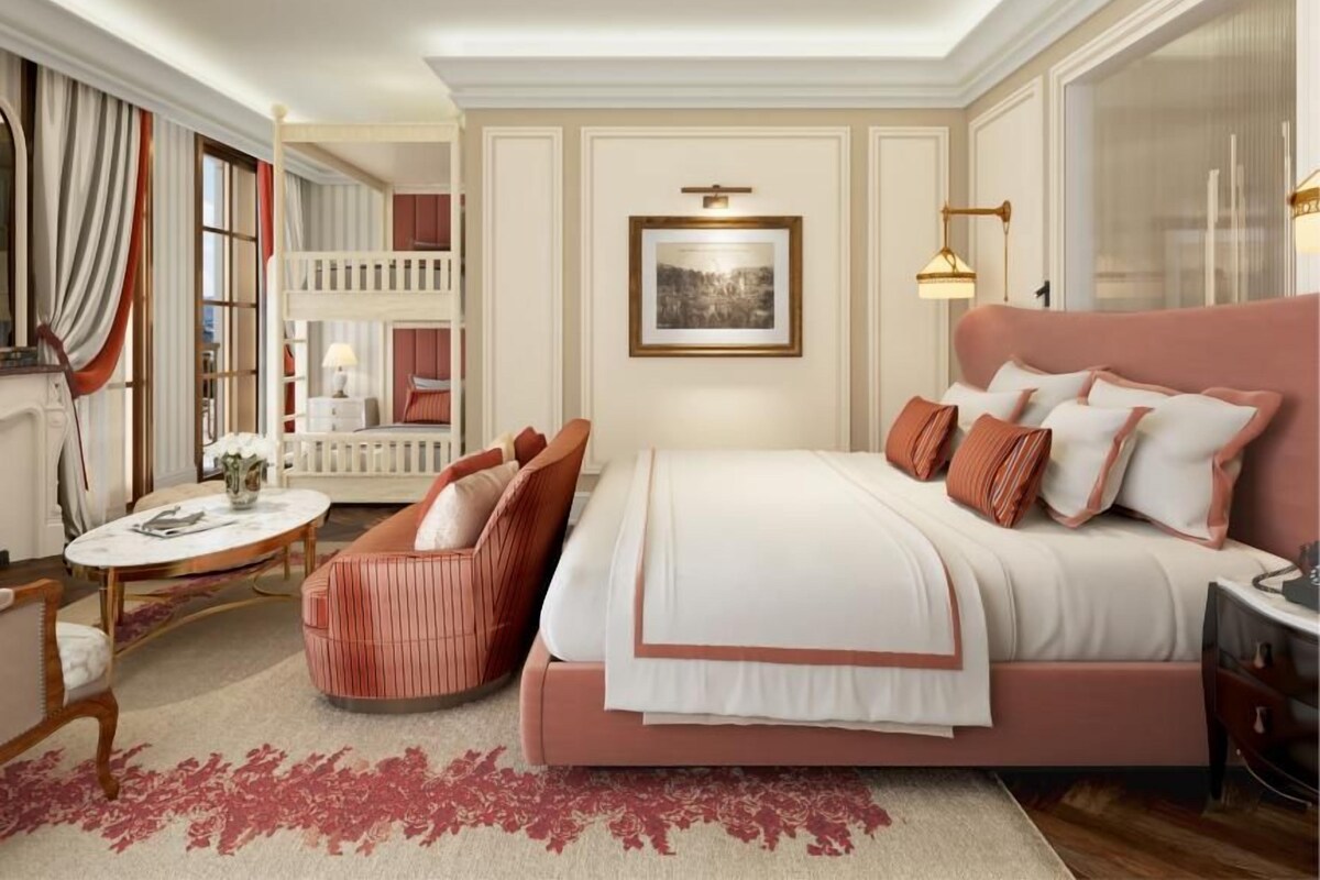 A bedroom with a large bed, a chair, a desk, and a window.