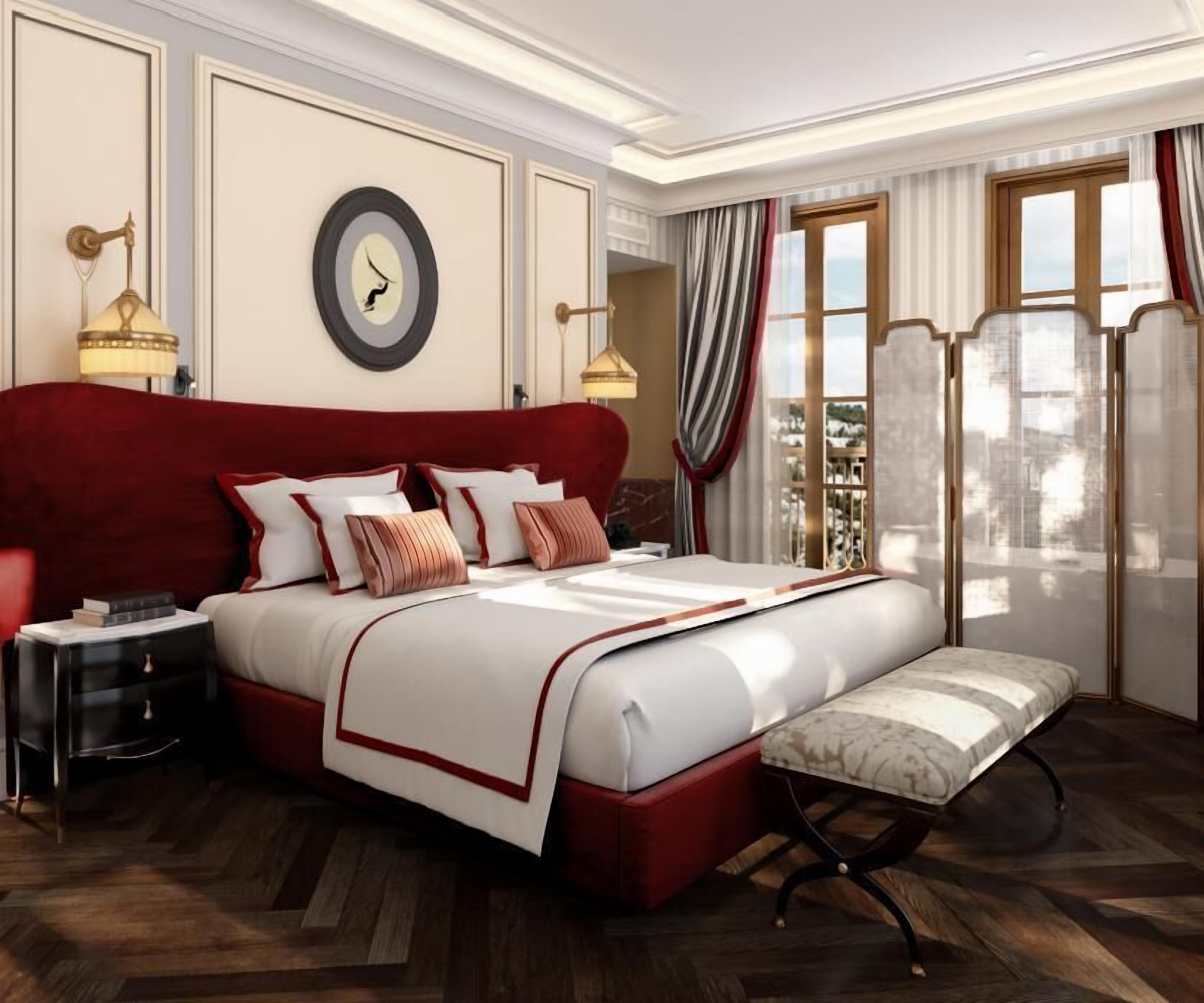 Een ruime slaapkamer met een groot bed, nachtkastjes, een bankje en uitzicht op de stad.