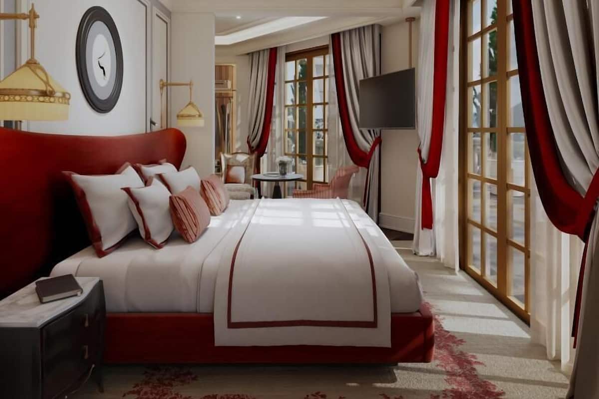A spacious bedroom with a large bed, a bedside table, a TV, and a window with curtains.